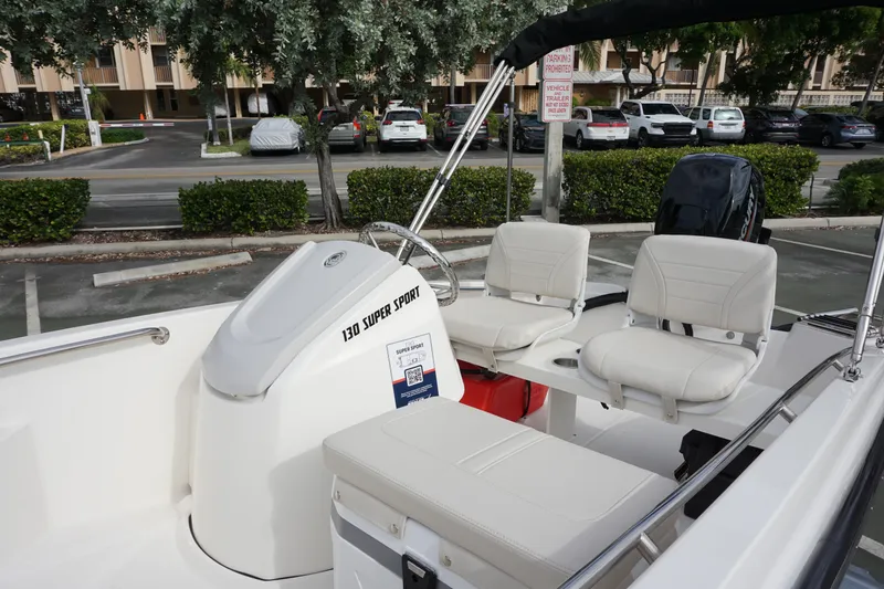 Slide: The Image of 2026 Boston Whaler 130 Super Sport boat with white seating and console, parked outdoors. - 7