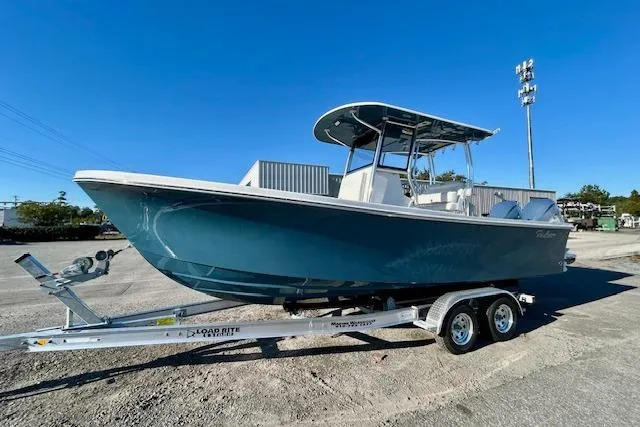 Slide: The Image of 2026 Pair Customs 24 Center Console DV Offshore boat on trailer, blue hull, sunny day. - 2