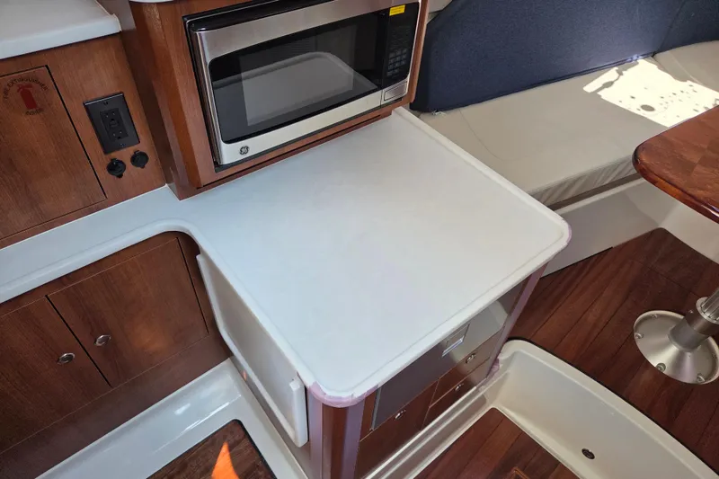 Slide: The Image of Interior of 2026 Pursuit OS 325 Offshore boat with microwave and wooden cabinetry. - 29
