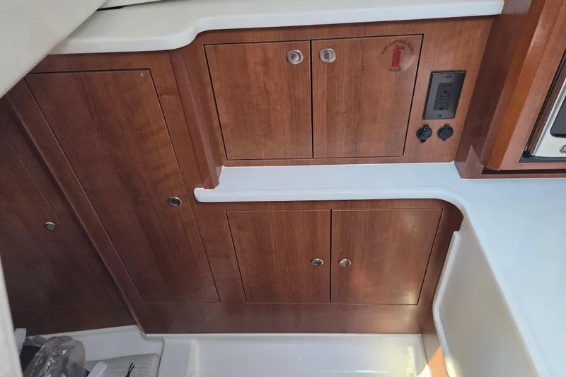 Slide: The Image of Interior cabinetry of 2026 Pursuit OS 325 Offshore boat, featuring wood finish and electrical outlets. - 30