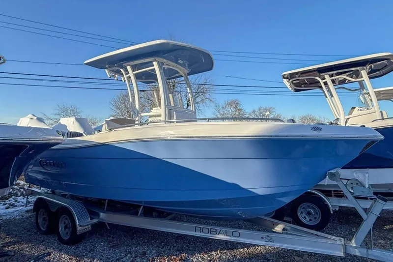 The Image of 2024 Robalo R222 Explorer boat on trailer, blue hull, clear sky background. - 1
