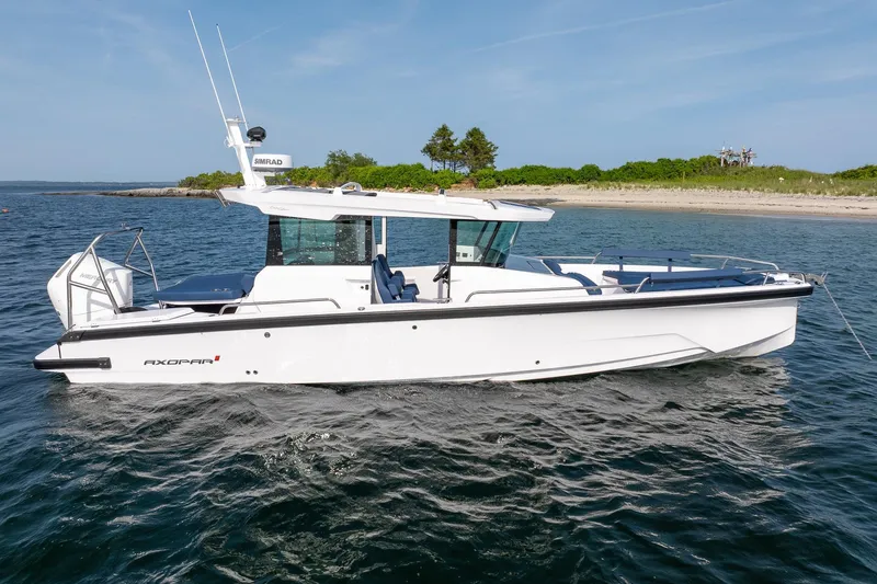 Slide: The Image of 2026 Axopar 29 Cross Cabin boat on calm water near a sandy shoreline. - 8