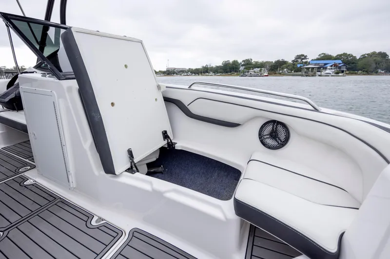 Slide: The Image of 2017 Yamaha Boats SX210 interior with open storage compartment and speaker, docked by the water. - 15