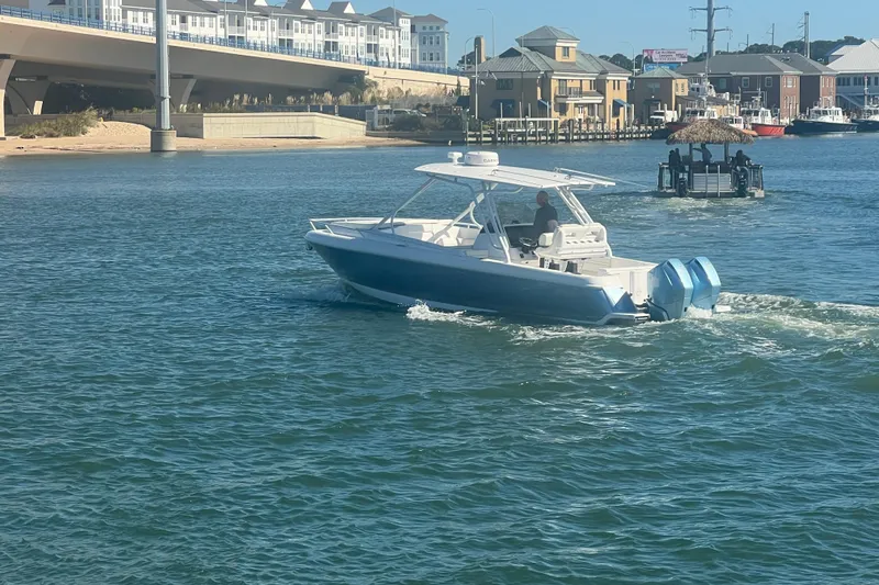 Slide: The Image of 2022 Intrepid 327-I CC boat cruising on a sunny waterfront near a bridge and buildings. - 63