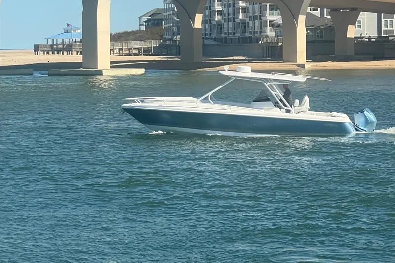 Slide: The Image of 2022 Intrepid 327-I CC boat cruising under a bridge near a sandy shore. - 64
