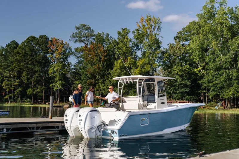 Slide: The Image of 2026 Sea Hunt Ultra 285 Coffin Box boat docked on a serene lake with people boarding. - 26