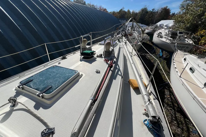 Slide: The Image of 1986 Victoria 34 Sloop sailboat on land, surrounded by other boats and a large building. - 16