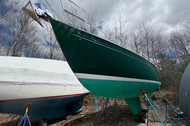 Slide: The Image of 1986 Victoria 34 Sloop sailboat on stands, green hull, outdoors, cloudy sky. - 44