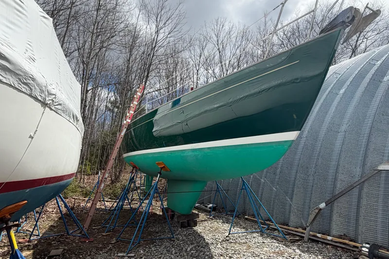 Slide: The Image of 1986 Victoria 34 Sloop sailboat on stands, surrounded by trees and a storage shelter. - 45