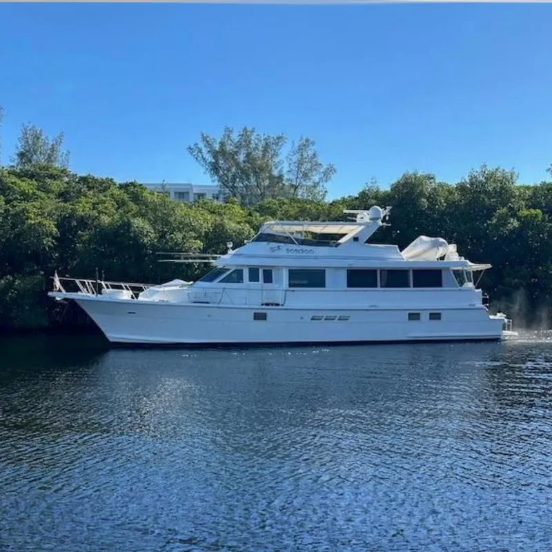The Image of 1998 Hatteras 70 Cockpit Motor Yacht on calm water, surrounded by lush greenery. - 0