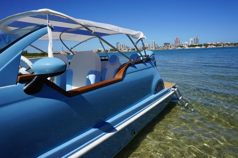Slide: The Image of Blue Fiat 500 Classic boat on clear water, city skyline in background, 2025 model. - 14