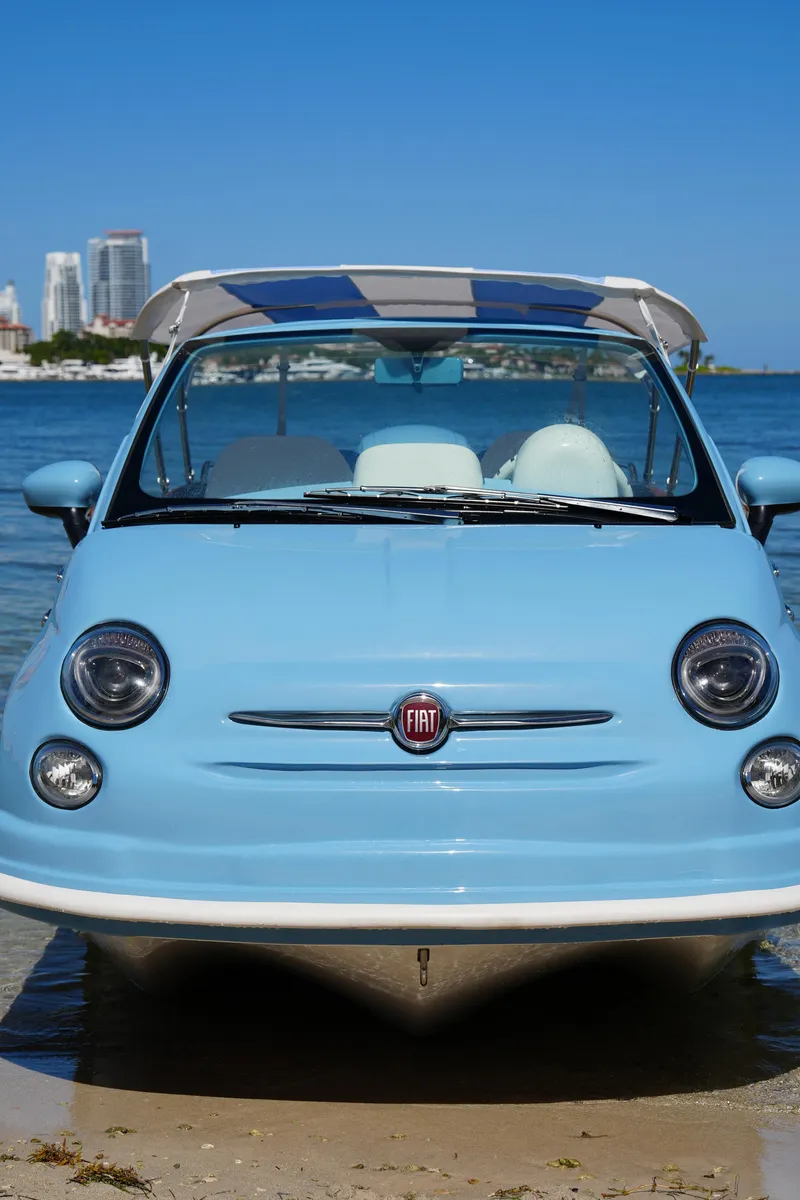 Slide: The Image of 2025 Car Off-shore Fiat 500 Classic, blue, parked by the water with city skyline. - 5
