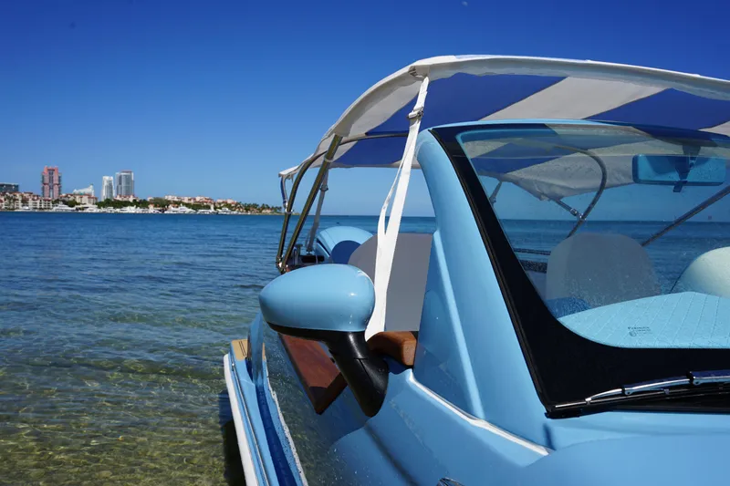 Slide: The Image of 2025 Car Off-shore Fiat 500 Classic on water, blue sky, city skyline in background. - 6