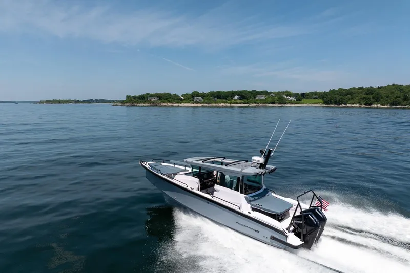 Slide: The Image of 2026 Axopar 29 Cross Cabin cruising on a serene lake with lush shoreline. - 14