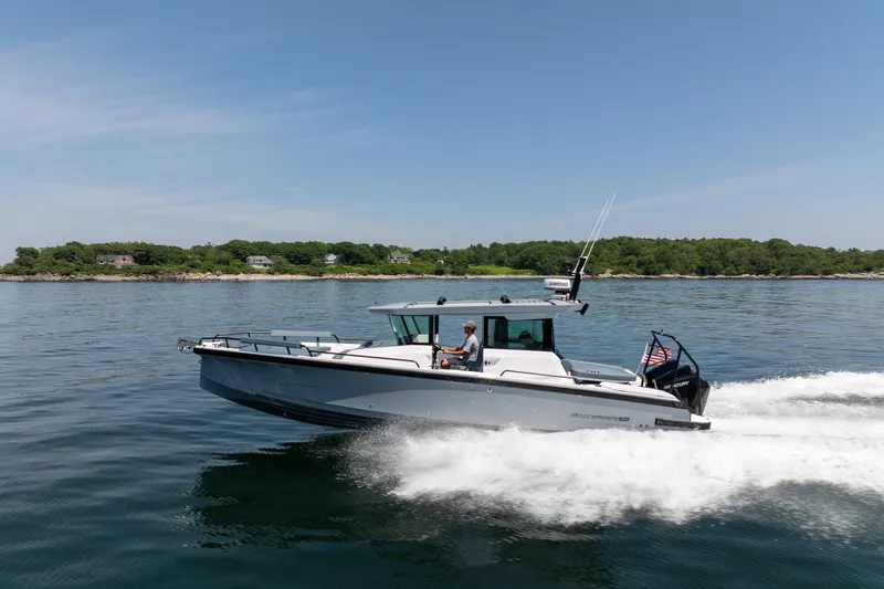 Slide: The Image of 2026 Axopar 29 Cross Cabin boat cruising on a calm lake with scenic shoreline. - 15