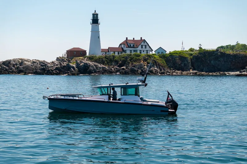 Slide: The Image of 2026 Axopar 29 Cross Cabin boat near a scenic lighthouse and rocky coastline. - 4
