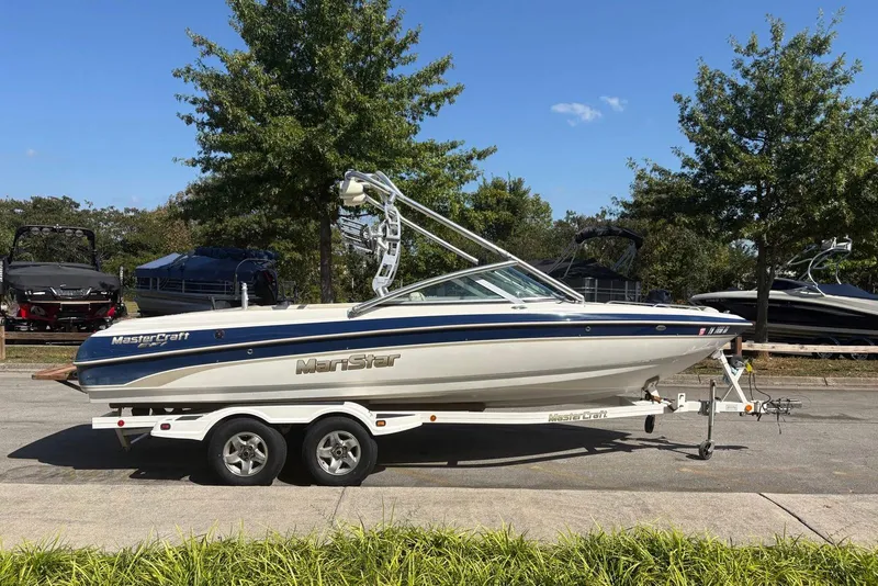 The Image of 2003 MasterCraft MariStar 230 SV boat on trailer, parked outdoors with trees in background. - 0