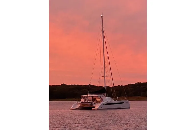 Slide: The Image of Seawind 1600 catamaran, 2022 model, anchored at sunset with pink sky backdrop. - 2
