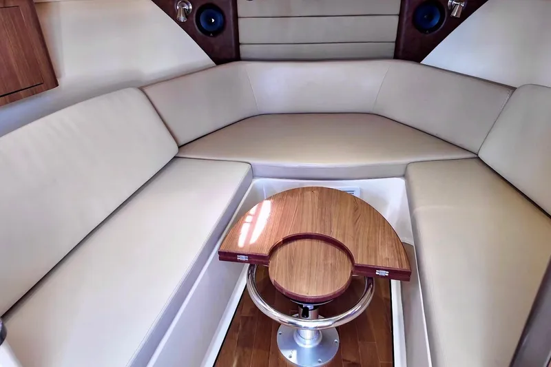 Slide: The Image of 2015 Boston Whaler 315 Conquest cabin interior with beige seating and wooden table. - 10