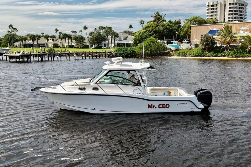 Slide: The Image of 2015 Boston Whaler 315 Conquest boat named "Mr. CEO" on a scenic waterway. - 2