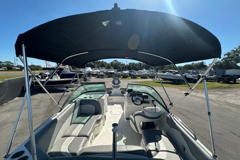 Slide: The Image of 2021 NauticStar 203 DC boat interior with canopy, parked in a marina under clear blue sky. - 16