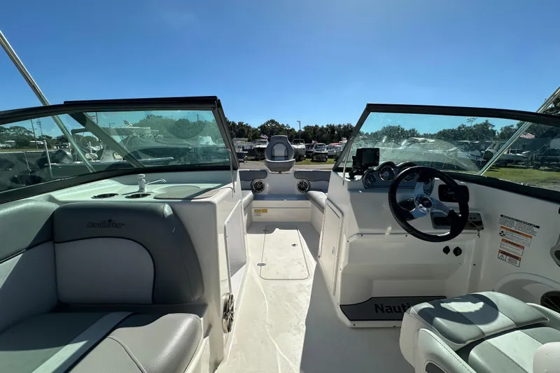 Slide: The Image of 2021 NauticStar 203 DC boat interior with steering wheel and seating under clear blue sky. - 24