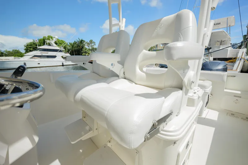 Slide: The Image of 2015 Sailfish 320 CC boat with white cushioned seating and steering wheel, docked near yachts. - 10