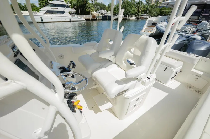 Slide: The Image of 2015 Sailfish 320 CC boat interior with white seating and steering wheel, docked near yachts. - 19