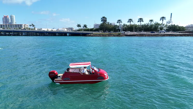 Slide: The Image of Red Fiat 500 Classic boat on blue water, palm trees in background, 2025 model. - 1