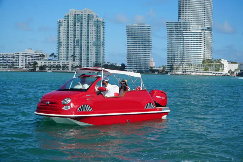 Slide: The Image of Red Car Off-shore Fiat 500 Classic boat on water, city skyline in background, 2025 model. - 2