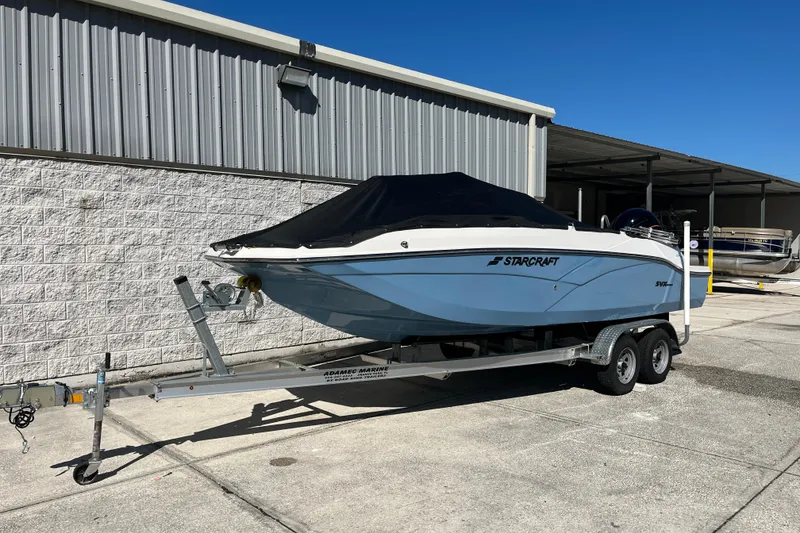 The Image of 2026 Starcraft SVX 211 OB boat on trailer, parked outdoors under clear blue sky. - 1