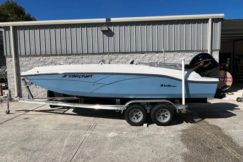 Slide: The Image of 2026 Starcraft SVX 211 OB boat on trailer, parked outside a metal building. - 6