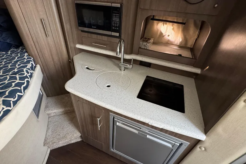 Slide: The Image of 2020 Rinker 320 EX boat interior kitchen with sink, stove, and microwave. - 19