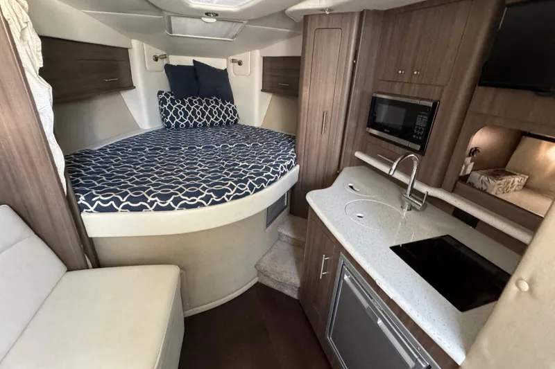 Slide: The Image of 2020 Rinker 320 EX cabin interior with bed, kitchenette, and seating area. - 20