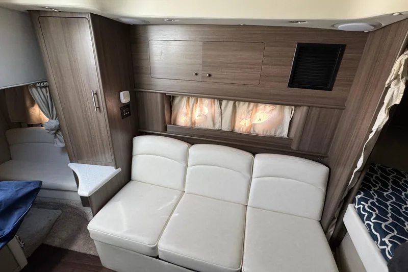Slide: The Image of 2020 Rinker 320 EX interior with white seating, wood cabinetry, and cozy curtains. - 22