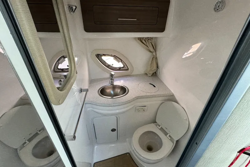 Slide: The Image of 2020 Rinker 320 EX boat bathroom with sink, toilet, and porthole windows. - 24