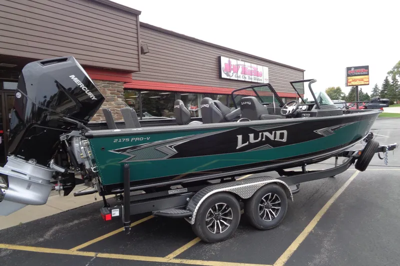 Slide: The Image of 2026 Lund 2175 Pro-V boat with Mercury engine on trailer, parked outside a building. - 2