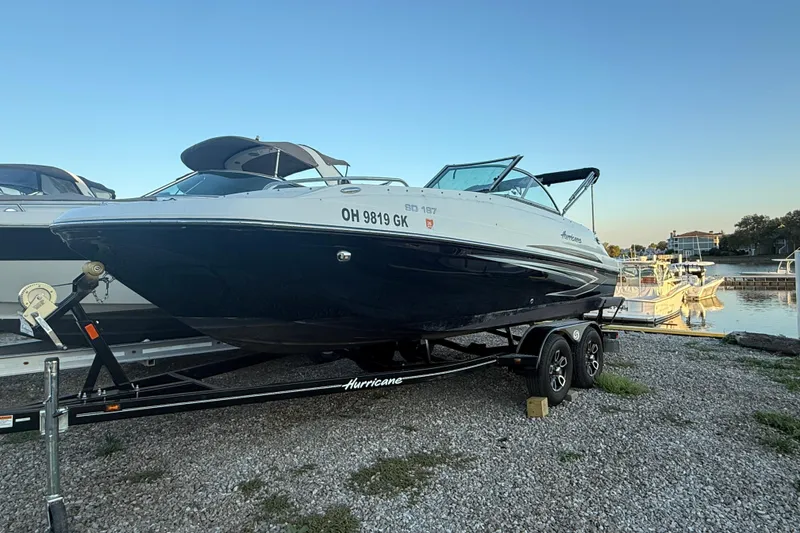 Slide: The Image of 2022 Hurricane SunDeck 187 IO boat on trailer by waterfront, clear sky background. - 5