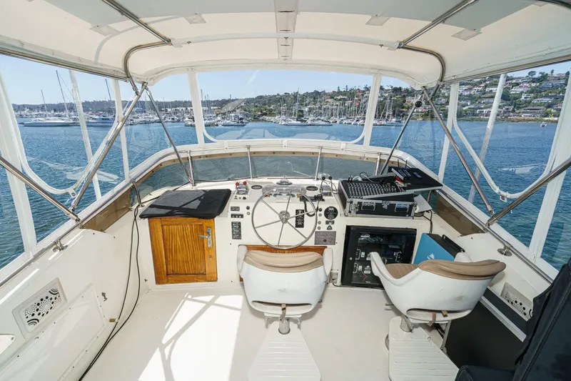 Slide: The Image of 1979 Hatteras 58 Motor Yacht helm with marina view, featuring dual captain chairs and navigation equipment. - 21
