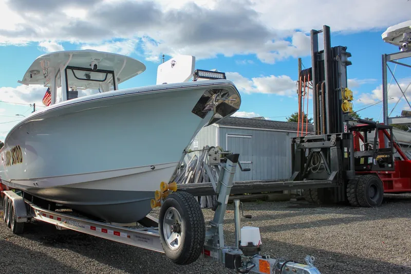 Slide: The Image of 2018 Sea Hunt Gamefish 30 boat on trailer, parked near forklift under blue sky. - 62