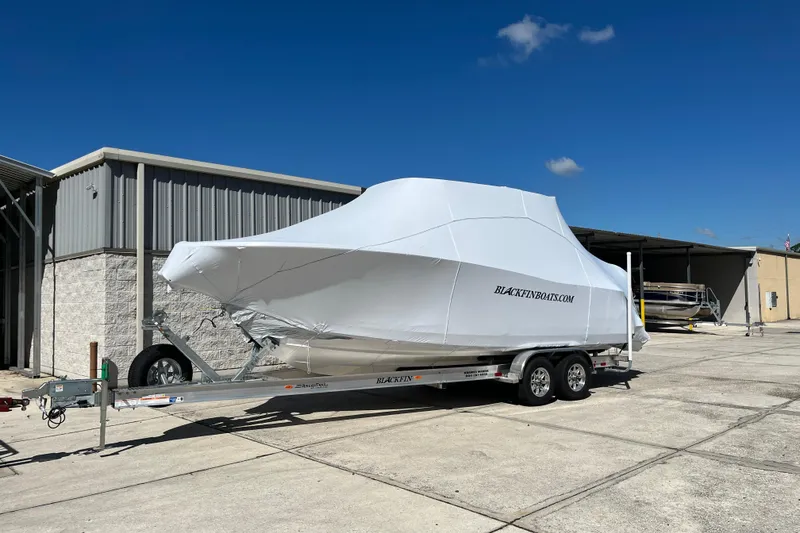 The Image of 2026 Blackfin 272 CC boat covered on a trailer outside a warehouse. - 0