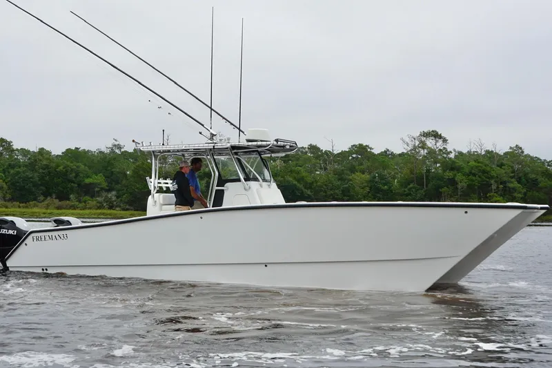 Slide: The Image of 2013 Freeman 33 boat cruising on water with lush green trees in the background. - 2