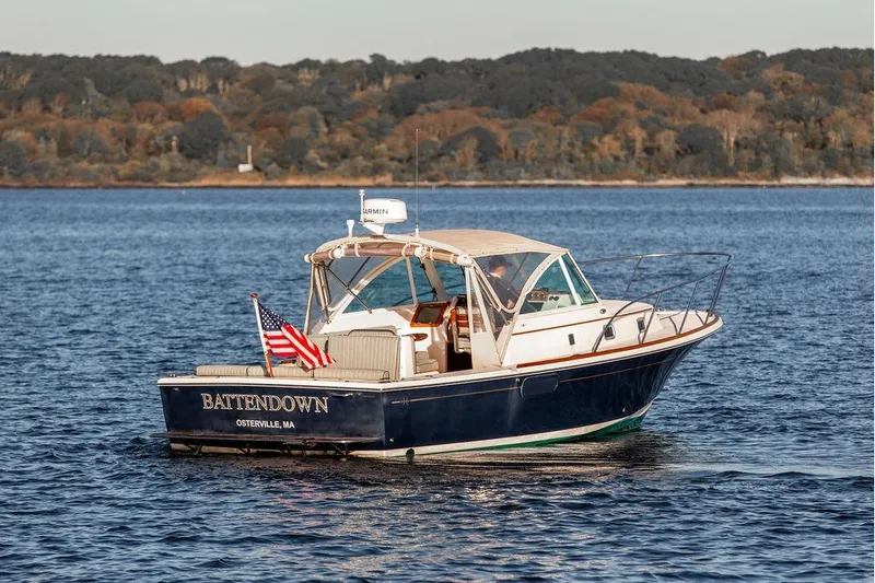Slide: The Image of 2007 Hunt Surfhunter 29 boat on water, displaying American flag, with wooded shoreline in background. - 3