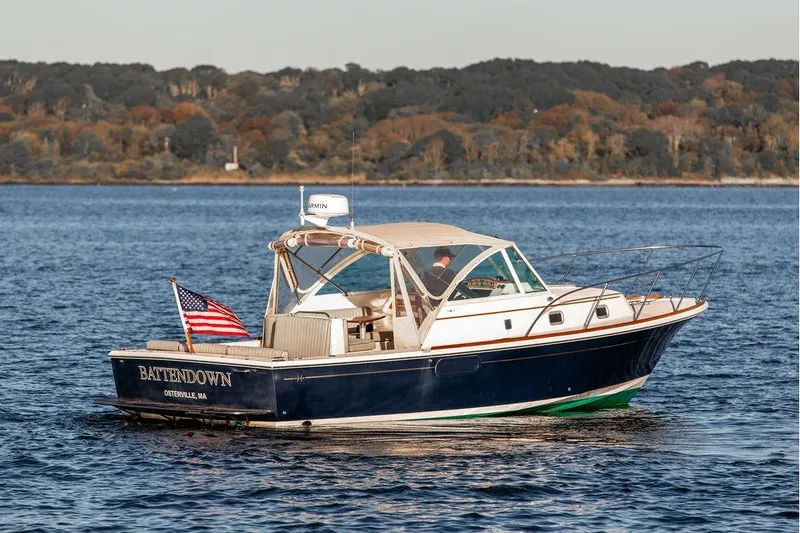 Slide: The Image of 2007 Hunt Surfhunter 29 boat on water, American flag, wooded shoreline background. - 9