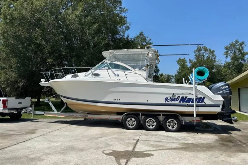 Slide: The Image of 2000 Wellcraft 290 Coastal boat on trailer, parked outdoors, clear sky background. - 1