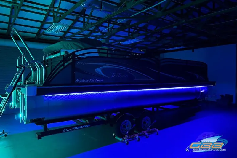Slide: The Image of 2026 JC 25 Neptoon LG pontoon boat with blue LED lights in a dimly lit garage. - 62