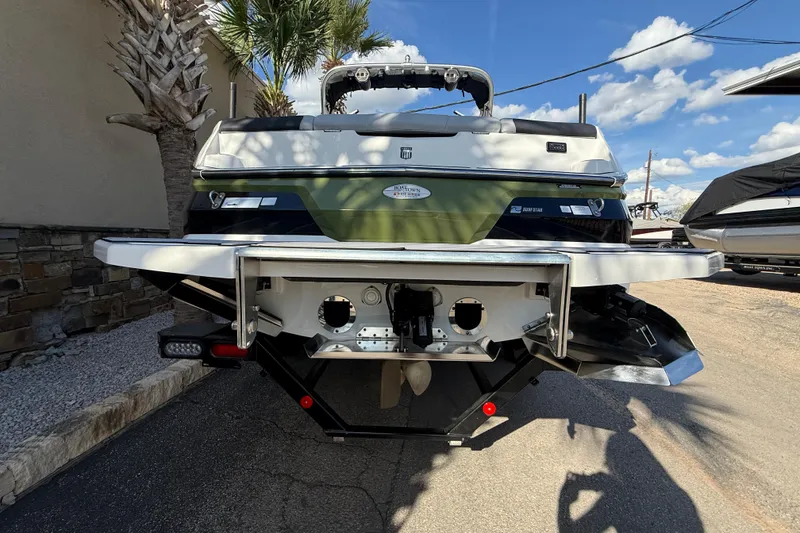 Slide: The Image of 2023 MasterCraft NXT24 boat rear view with green and white design, parked outdoors. - 6