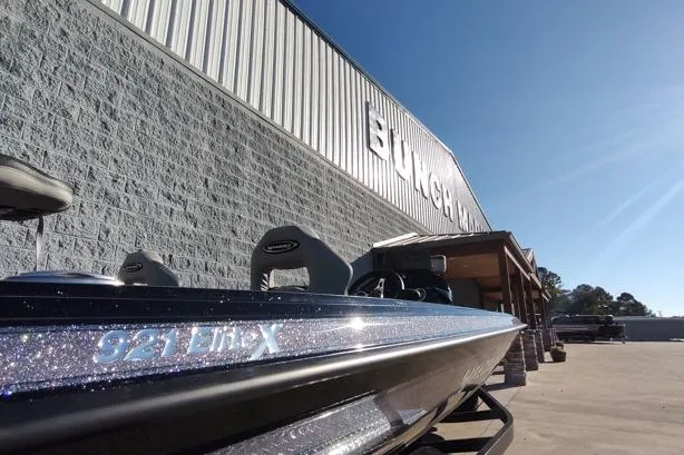 Slide: The Image of 2026 Phoenix 921 Elite X boat parked outside a large building under a clear blue sky. - 12