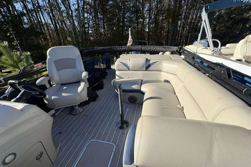 Slide: The Image of 2017 Berkshire 23 boat interior with beige seating and steering wheel, surrounded by trees. - 10