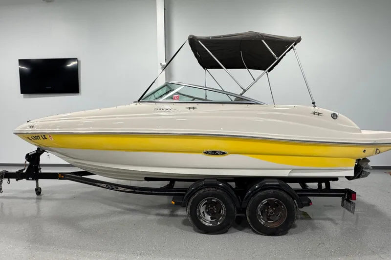 The Image of 2004 Sea Ray 200 Sundeck boat with yellow accents on a trailer indoors. - 1